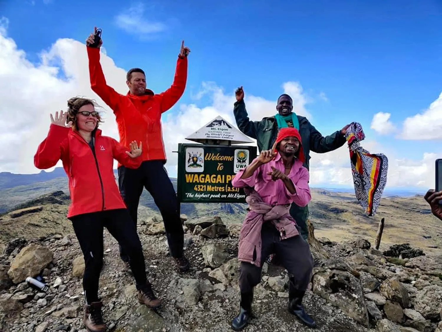 Hikers celebrating beside the Wagagai summit sign on Mount Elgon