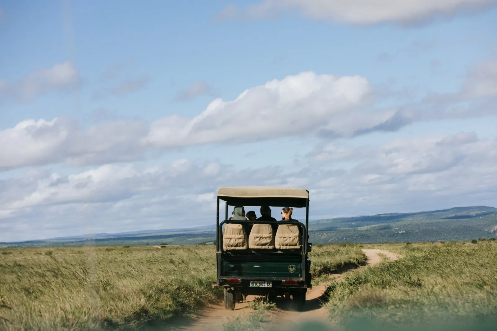 An open-sided safari vehicle with travellers on a dirt track across the plains