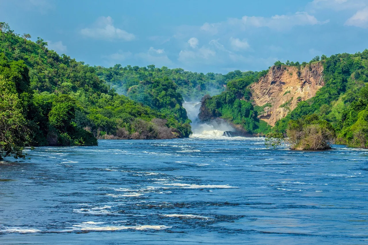A waterfall pouring through a rocky, forested gorge into a wide river